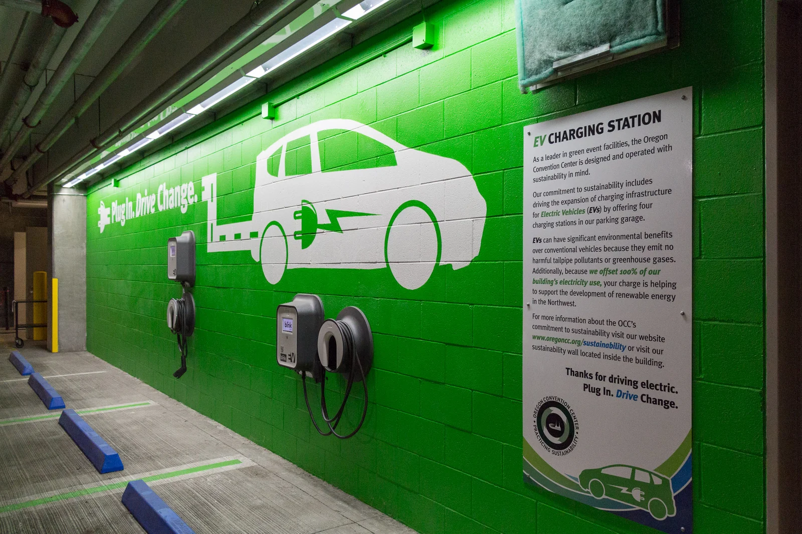 Two wall-mounted EV chargers with coiled cables beside marked bays in the Oregon Convention Center parking garage in Portland, USA.