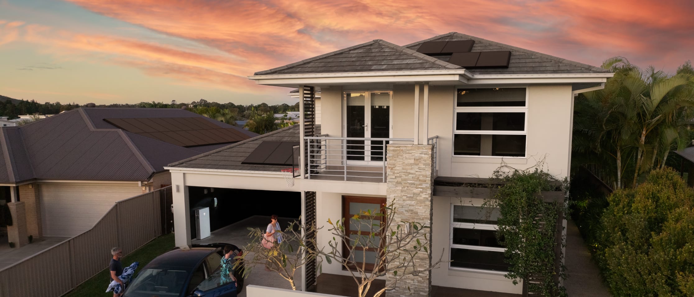Solar panels on a home with an electric car outside and a Tesla Powerwall in the garage