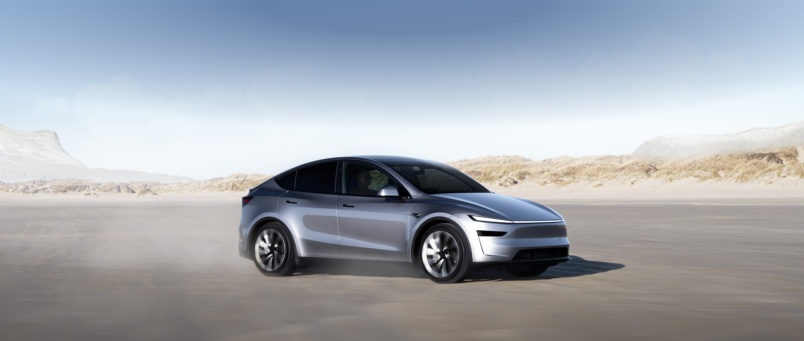Silver Tesla Model Y driving past coastal dunes in official Australian regional promotional photography