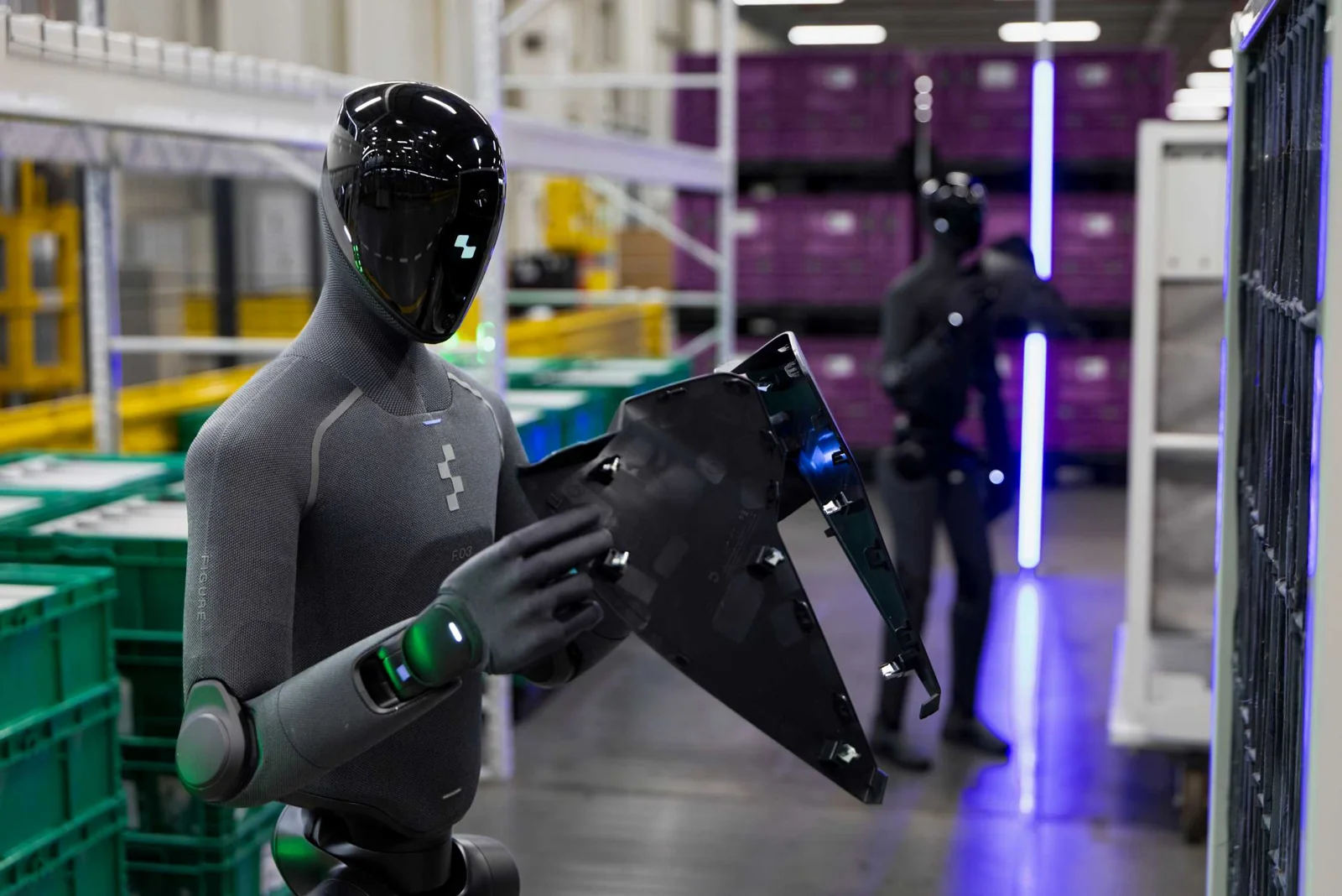 Figure 03 humanoid robot holding a component beside storage racks at BMW’s Spartanburg plant.